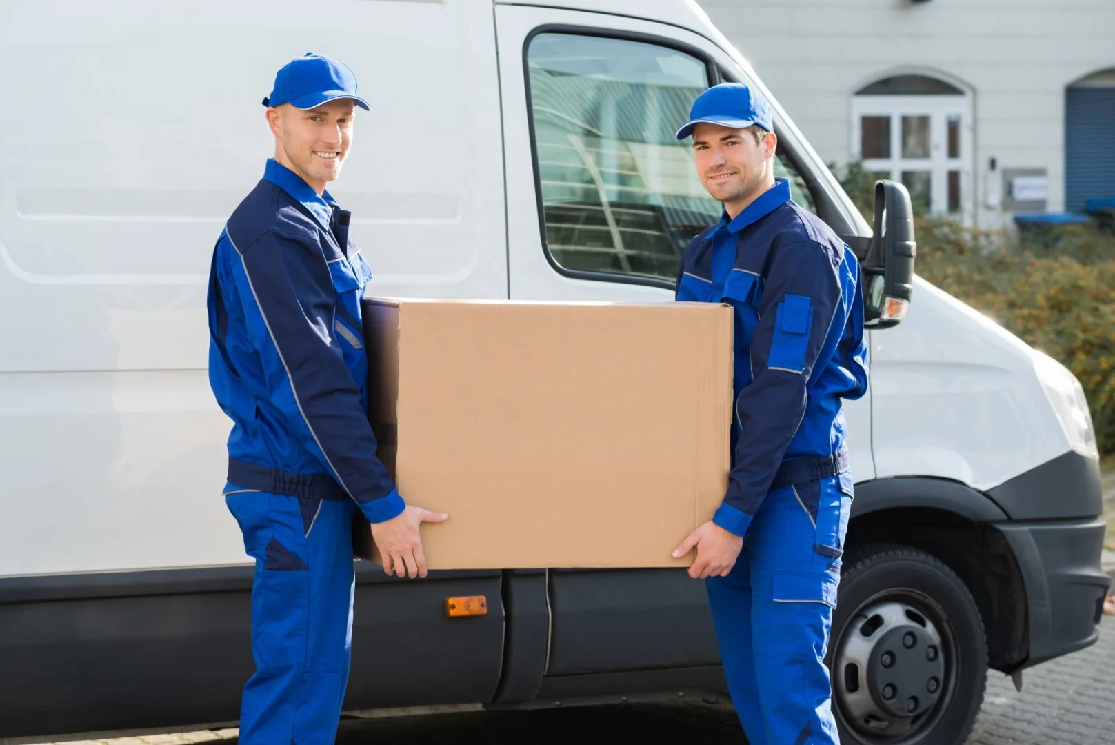 Reliable Movers in Action Professional movers in blue uniforms carrying a box near a moving van.