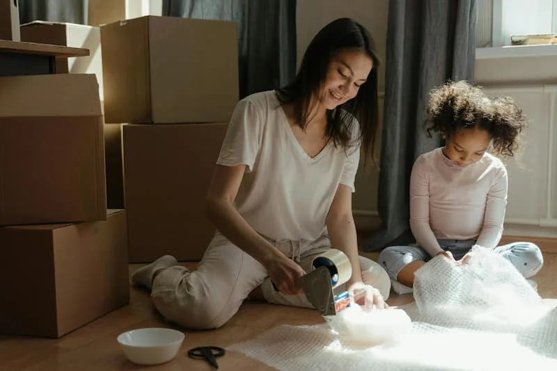 Packing for Relocation Woman and child packing bowls for moving, surrounded by boxes.
